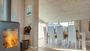 A modern interior with a wood-burning stove, a dining area with white chairs, and a wooden ceiling. - "Afrim" - 694m from the sea by Interhome (Hjørring)