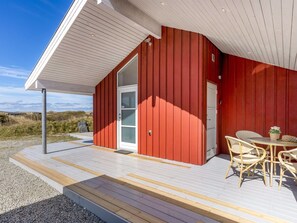 A modern red building with a glass door and a covered outdoor seating area with wicker furniture. - "Björnstjerne" - 400m from the sea by Interhome (Hjørring)