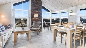 A spacious living area with a large dining table, comfortable seating, and a view of the landscape through large windows.
