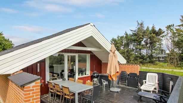Een overdekt terras buiten met een eettafel en stoelen, een grill en een barbecueplek.