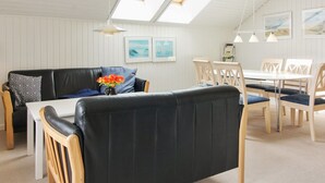 Een gezellige kamer met een zwarte leren bank, houten stoelen, een witte tafel en een dakraam.