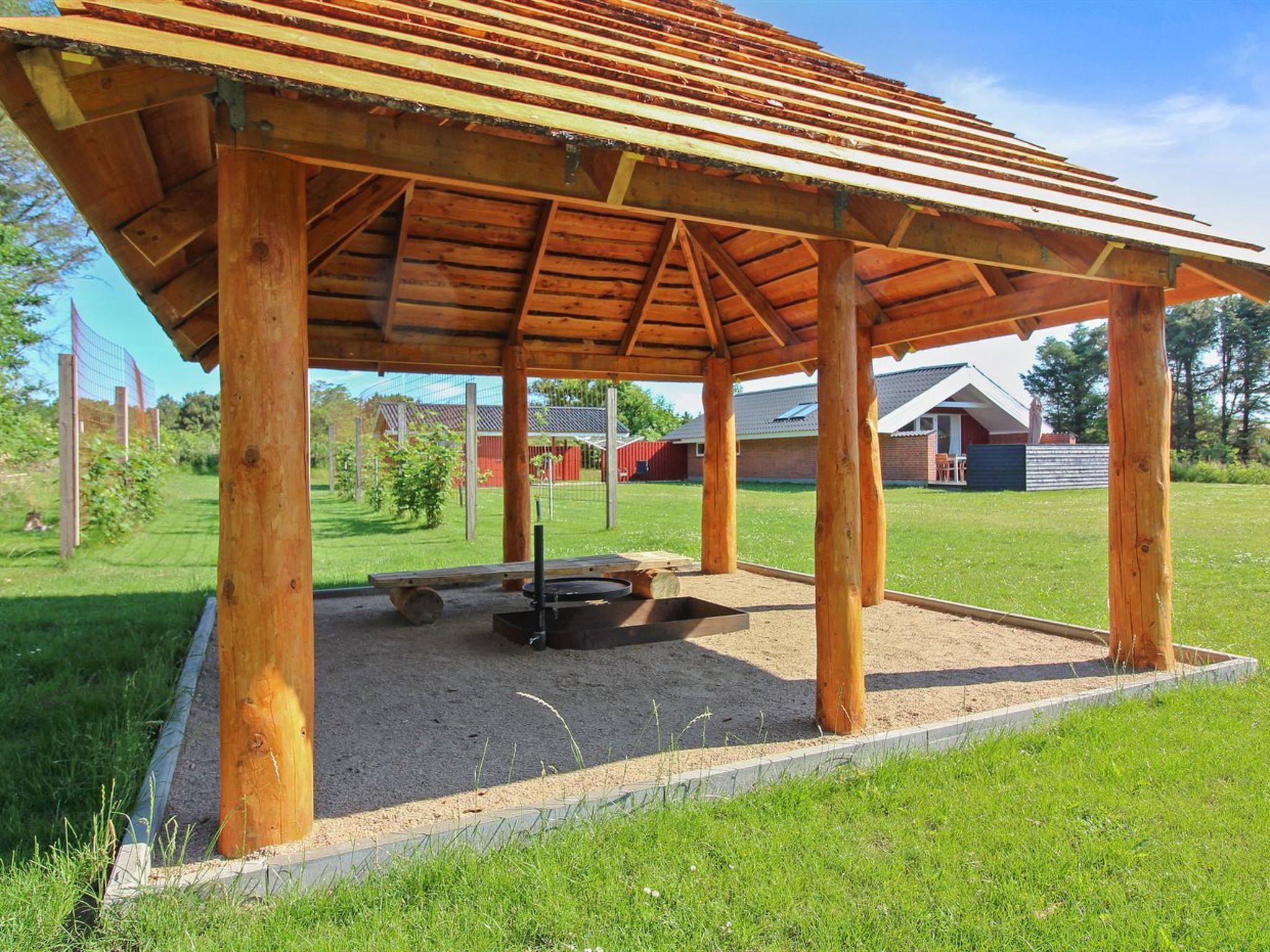 A wooden pavilion with a sloped roof, a fire pit, and a bench.