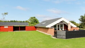 Een huis met twee verdiepingen, een rode schuur, een terras met buitenmeubilair en een verzorgd gazon.