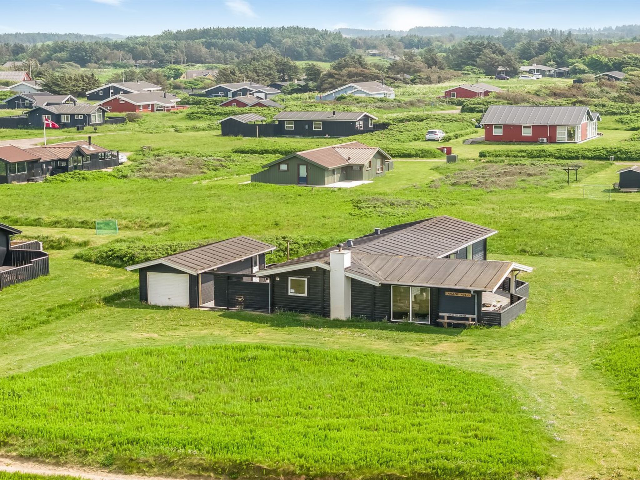Una zona residencial con varias casas, algunas con garajes integrados, en un paisaje verde bajo un cielo despejado.
