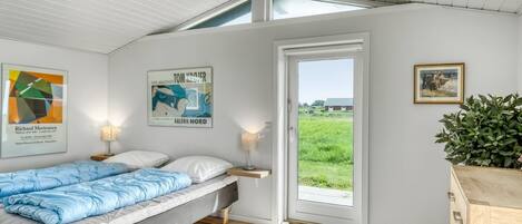 Ein Schlafzimmer mit einem Bett, zwei Wandlampen, einer Tür zu einem Balkon und zwei gerahmten Kunstwerken.