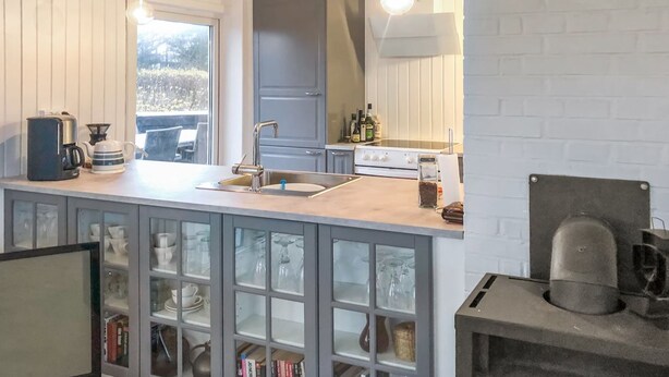 Une cuisine dotée d’un îlot central intégré, d’une cuisinière et d’un évier. Des luminaires suspendus et une fenêtre laissent entrer la lumière naturelle.