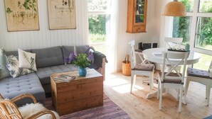 Un salon chaleureux avec un canapé gris, une table basse en bois et un coin repas comprenant des chaises et une table blanches.