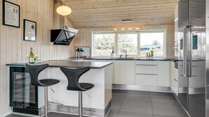 Une cuisine moderne dotée d’un îlot central, de deux tabourets de bar, d’appareils électroménagers en acier inoxydable et d’une fenêtre laissant entrer la lumière naturelle.