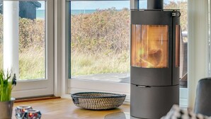 Un intérieur moderne avec un poêle à bois, de grandes fenêtres et une vue sur l’extérieur.