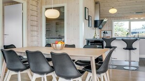 Une cuisine moderne aux murs en bois, un coin repas avec une table en bois et des chaises noires, et un bar avec des tabourets.