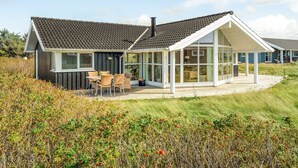 Une maison moderne dotée d’une grande extension en verre, d’un patio avec mobilier d’extérieur et d’un jardin verdoyant.