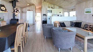 Un intérieur moderne avec un plafond en bois, un coin repas comprenant une table et des chaises, un canapé gris et une cuisine en arrière-plan.