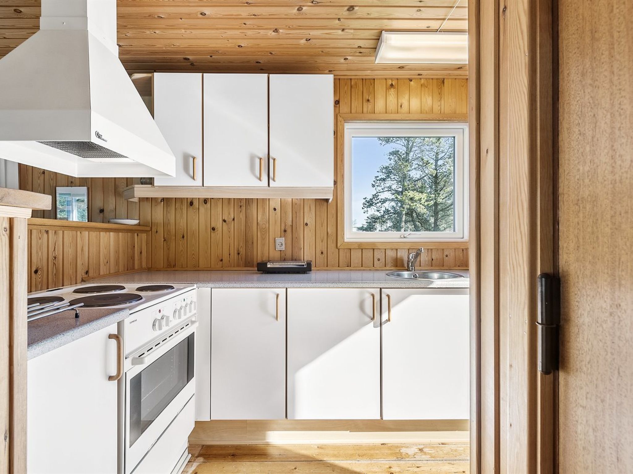 Een moderne keuken met witte kasten, een fornuis en een raam met uitzicht op bomen.