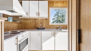 A modern kitchen with white cabinets, a stove, and a window overlooking trees. - "Freija" - 719m from the sea by Interhome (Hjørring)