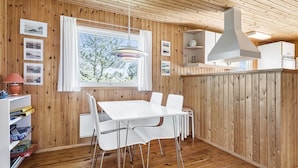 A wooden-paneled room with a white table and chairs, a window with curtains, and a hanging light fixture. - "Freija" - 719m from the sea by Interhome (Hjørring)