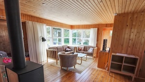 A cozy cabin interior with a wooden floor, a sofa set, a fireplace, and large windows. - "Freija" - 719m from the sea by Interhome (Hjørring)