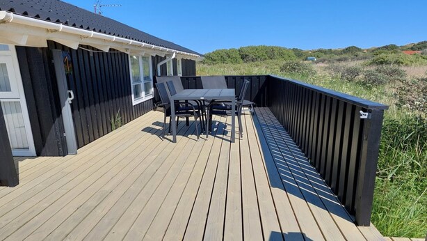 Una terraza de madera con una mesa, sillas, un ventanal y vistas del paisaje circundante.