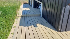 Una terraza de madera que conduce a un edificio con fachada oscura y techo blanco.