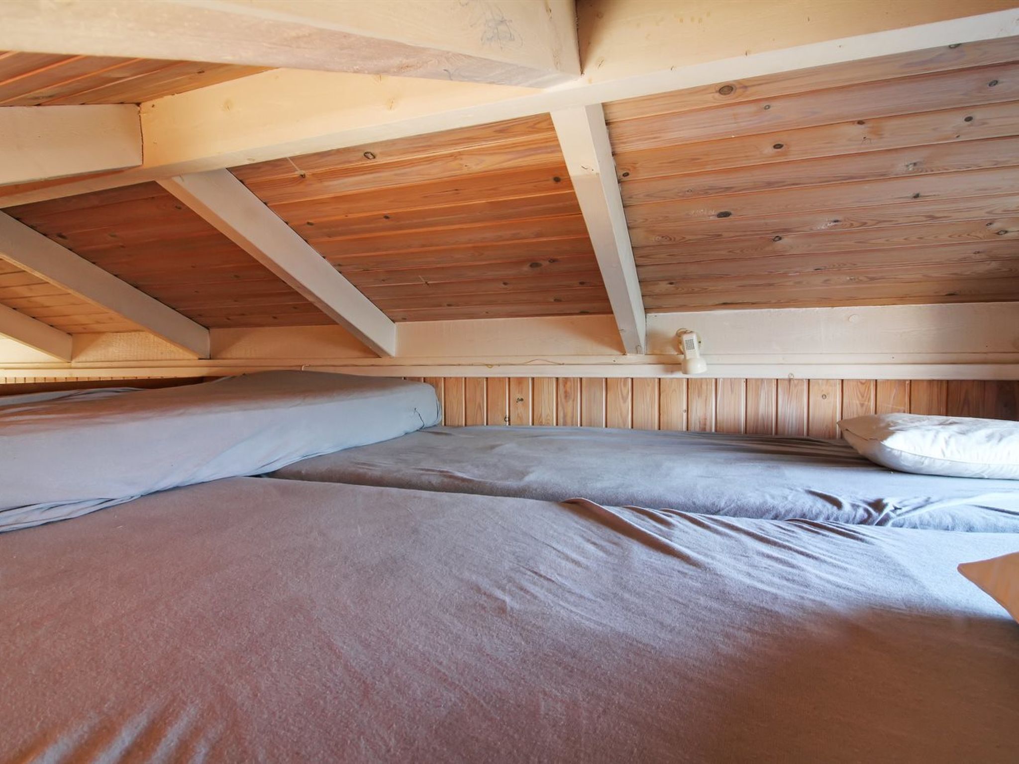 Ein Schlafzimmer im Loft-Stil mit freiliegenden Holzbalken und schräg versiegelter Decke.