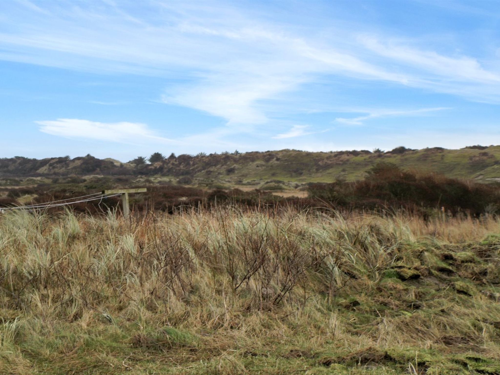 Paisaje rural con colinas onduladas, una valla de madera y vegetación escasa.