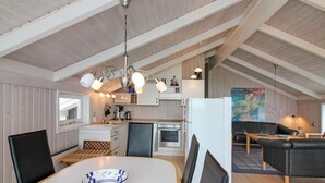 Una cocina moderna con armarios blancos, una zona de comedor con mesa y sillas blancas, y un dormitorio en entrepiso con sofá de cuero negro.