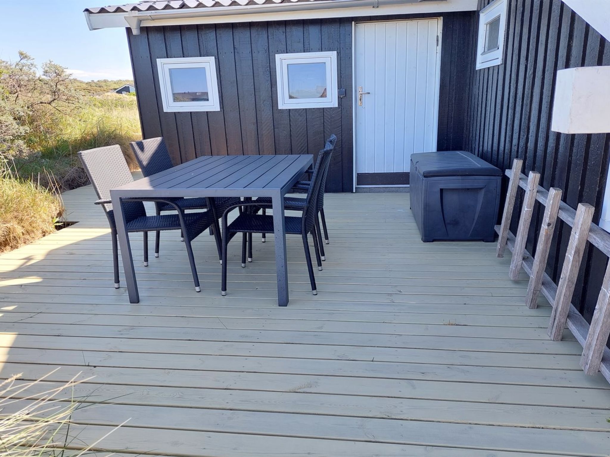 Eine Holzterrasse mit Tisch und Stühlen, ein kleiner Sitzbereich im Freien und ein Gebäude mit zwei Fenstern und einer Tür.