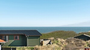 Een landgoed aan de kust met een groen gebouw, een houten boot en uitzicht op zee.