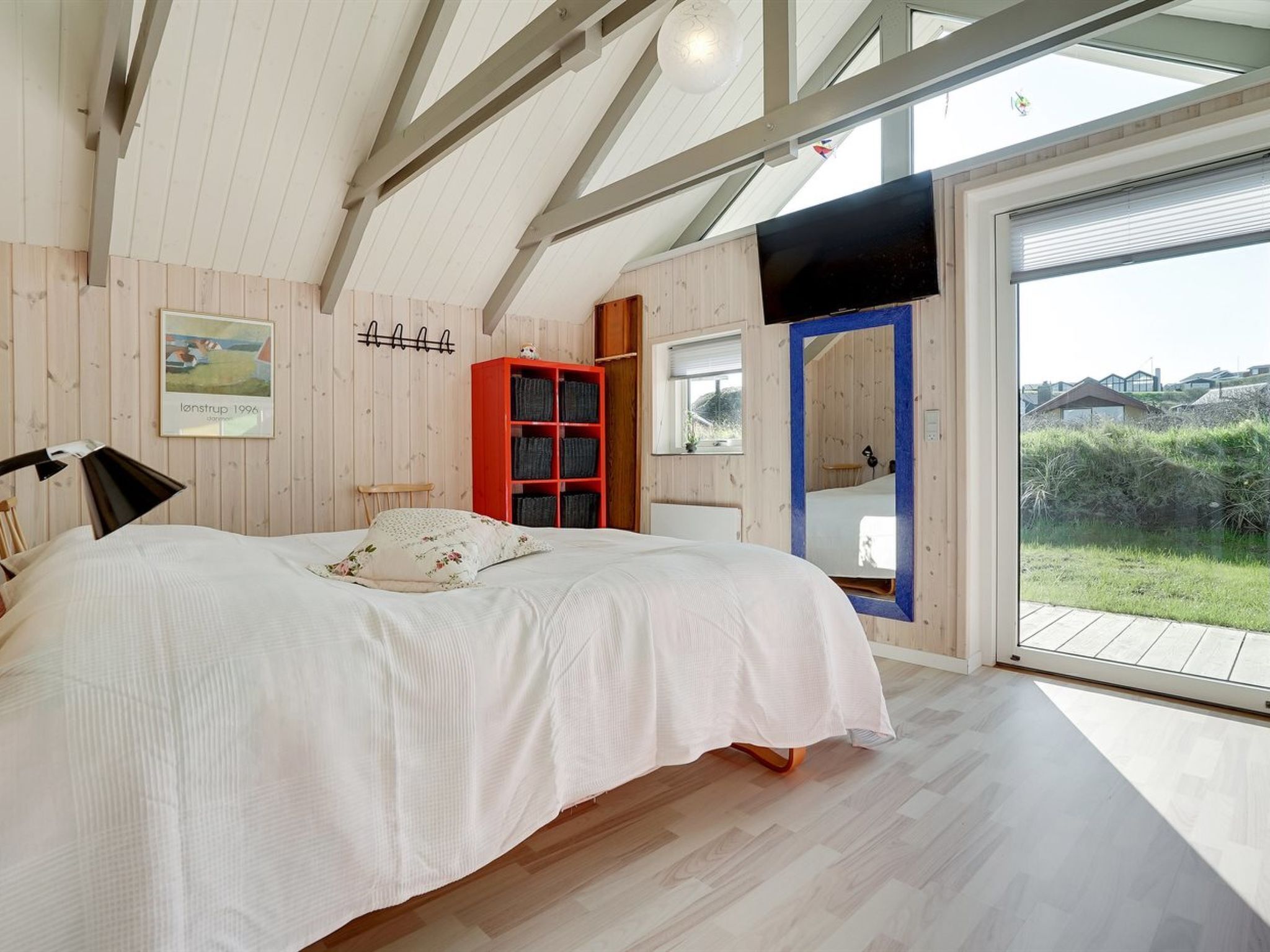 Un dormitorio con cama, un mueble de almacenamiento rojo, techo de madera y un ventanal grande.