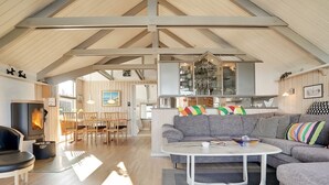 Een ruime woonkamer met een hoge plafond, een open haard, een eethoek en een bank met kleurrijke kussens.