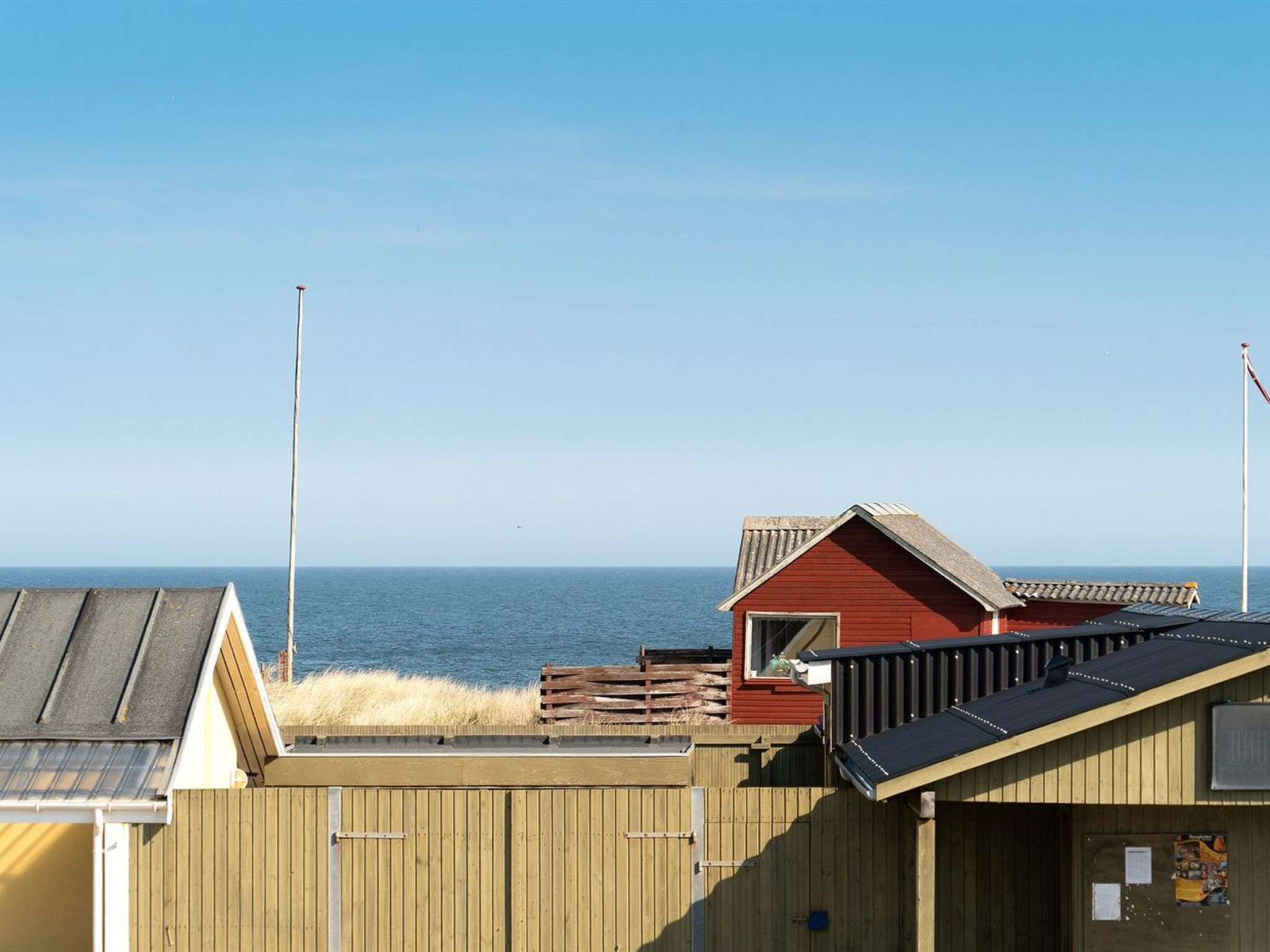 Un edificio costero con techo rojo y terraza de madera, con vista al mar.