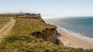 A coastal landscape with a cliff, beach, and a lighthouse in the distance.