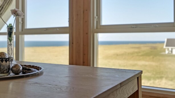 A wooden table with a decorative glass vase and ornaments, positioned near large windows overlooking a flat landscape.