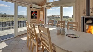 A modern dining area with a large table, wooden chairs, and a view of the beach.