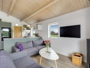 A compact living space with a kitchenette, a sofa, a coffee table, and a TV mounted on the wall.