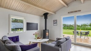 A modern living room with a fireplace, grey sofas, a round coffee table, and a large sliding glass door to a deck.