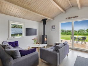 A modern living room with a fireplace, grey sofas, a round coffee table, and a large sliding glass door to a deck.