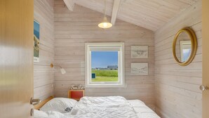 A bedroom with a wooden ceiling, a window with a view, a bed, a bedside table, and a mirror.