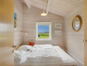 A bedroom with a wooden ceiling, a window with a view, a bed, a bedside table, and a mirror.