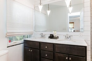 A bathroom with a white vanity, dark cabinets, a large mirror, and a window with blinds. - Cozy 3BR Home 4 Min From ND (SOuth Bend)
