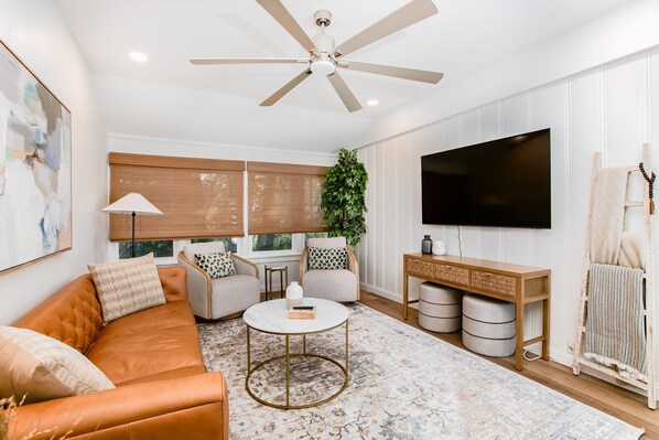 A modern living room with a leather sofa, a round coffee table, and a flat-screen TV mounted on the wall. - Cozy 3BR Home 4 Min From ND (SOuth Bend)