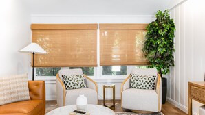Uma sala de estar com sofá, duas poltronas, uma mesa de centro, abajur e uma planta grande.