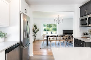 Une cuisine moderne dotée d’appareils électroménagers en acier inoxydable, un coin repas avec une grande fenêtre et un lustre.