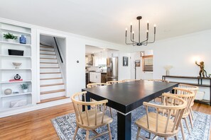 A modern kitchen with stainless steel appliances, a dining area with a black table and wooden chairs, and a staircase leading to an upper level.