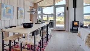Een modern interieur met een houten plafond, een eethoek met een grote tafel en stoelen, een open haard en grote ramen met uitzicht op het landschap.