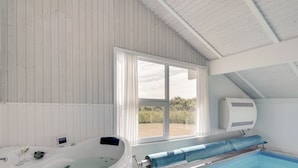 Ein moderner Innenpool mit Whirlpool, großen Fenstern und einem Deckenventilator.