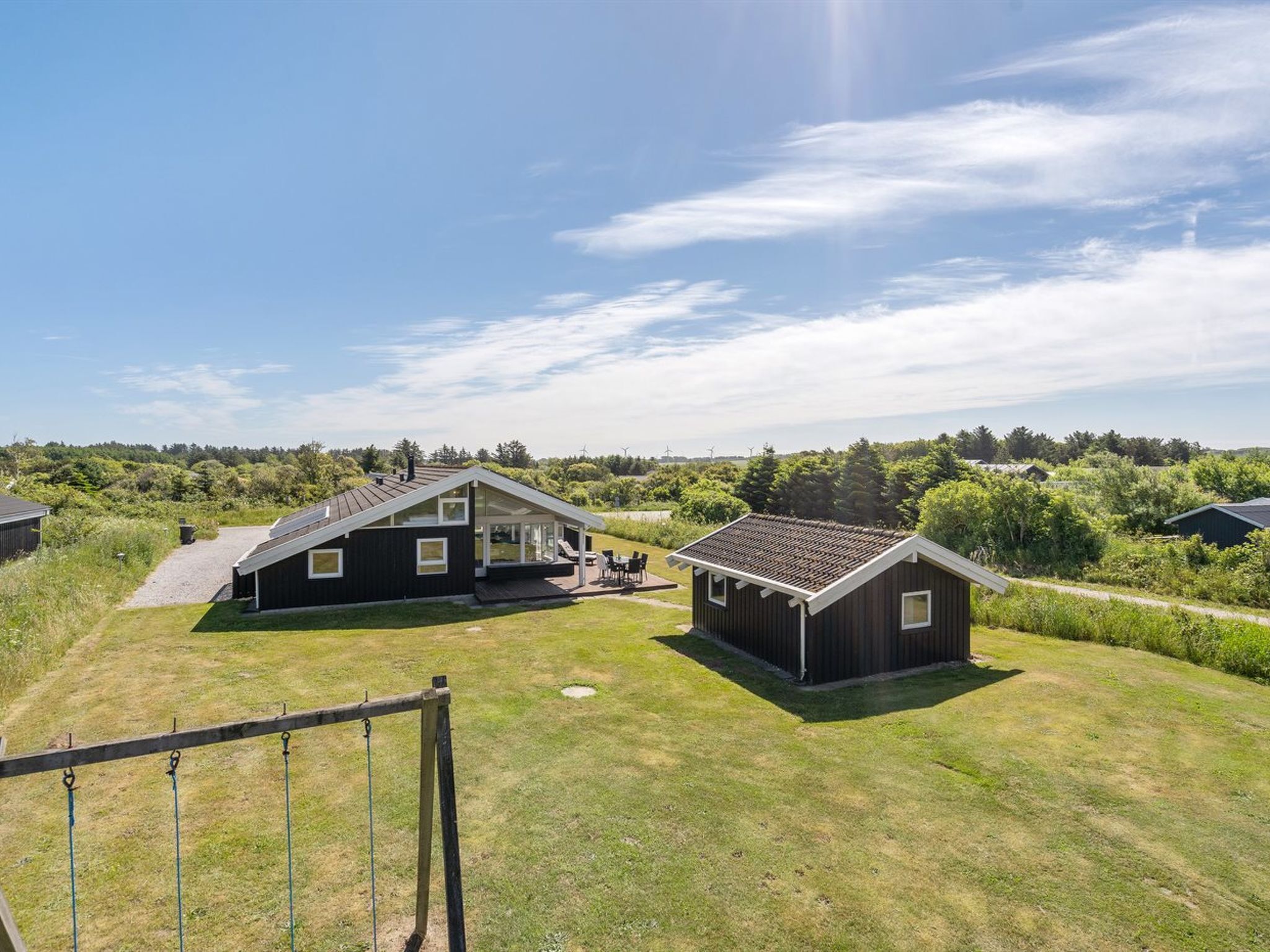 A modern house with a large patio, surrounded by a grassy yard and a wooden fence.