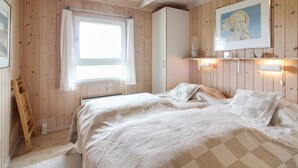 Une chambre avec des murs en bois, un lit recouvert d’une couette à carreaux, une fenêtre avec des rideaux, une échelle en bois et un tableau encadré accroché au mur.