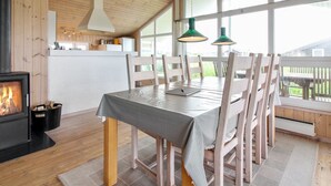 Un coin repas chaleureux avec une table et des chaises en bois, une cheminée et de grandes fenêtres donnant sur l’extérieur.