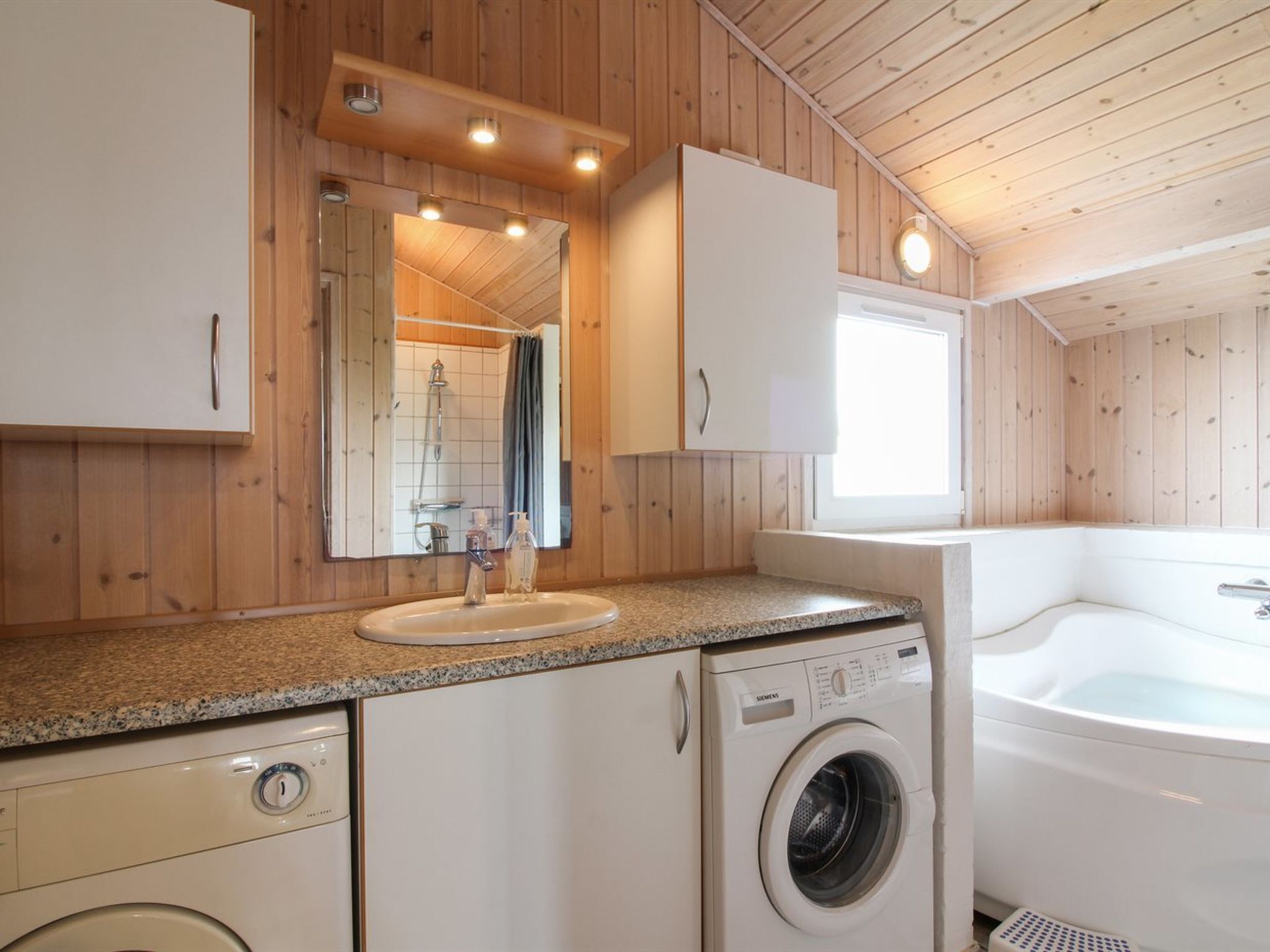 Ein kleines Badezimmer mit Holzwänden, einem Waschbecken, einer Waschmaschine und einer Badewanne.