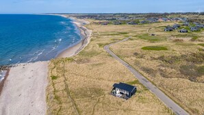 Vista aérea de una zona costera con playa, campos cubiertos de hierba y varias casas.